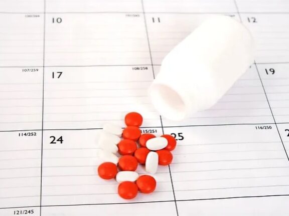 red and white pills spilling from a bottle onto a calendar
