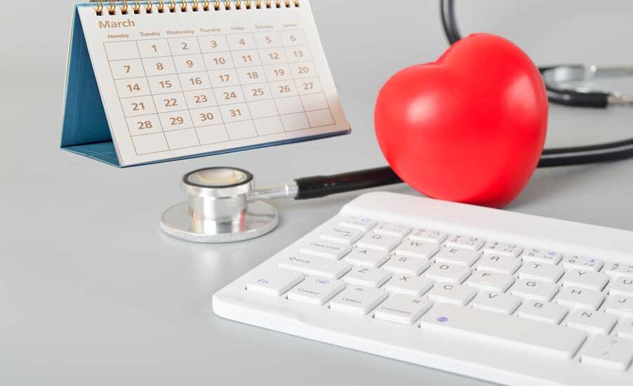 Computer keyboard, pastic red heart, stethoscope, and calendar on a table.