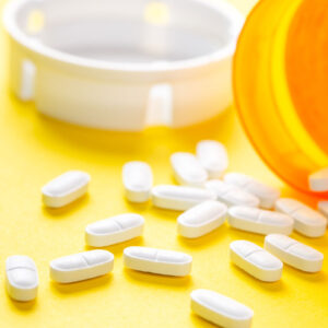 White pills on a yellow table with prescription bottle.